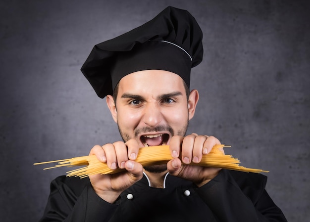 Foto ritratto di un cuoco in uniforme nera con spaghetti in mano su sfondo grigio