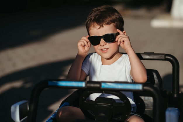 portrait of a child boy in sunglasses in a toy mini car in the park in summer