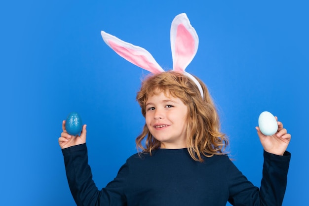 Portrait of child boy with easter eggs and bunny ears isolated on blue background