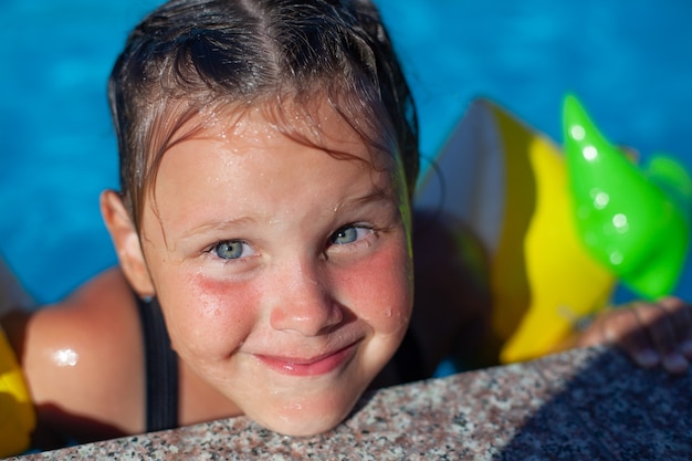 Portrait of child by pool little happy girl with wet hair makes faces at side of pool and enjoys war...