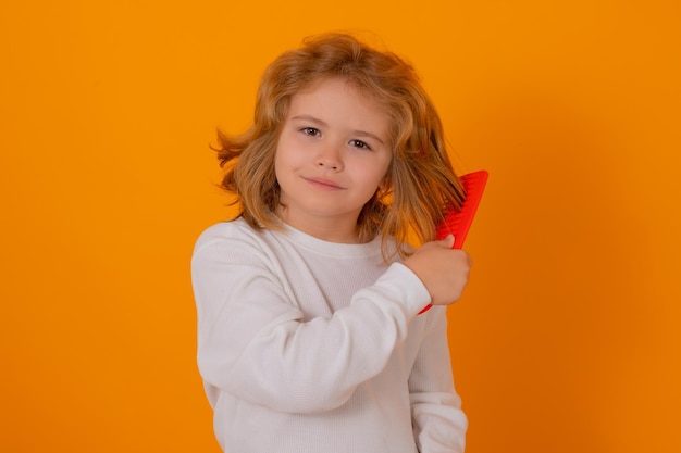 Photo portrait of child combing hair with comb on yellow studio background