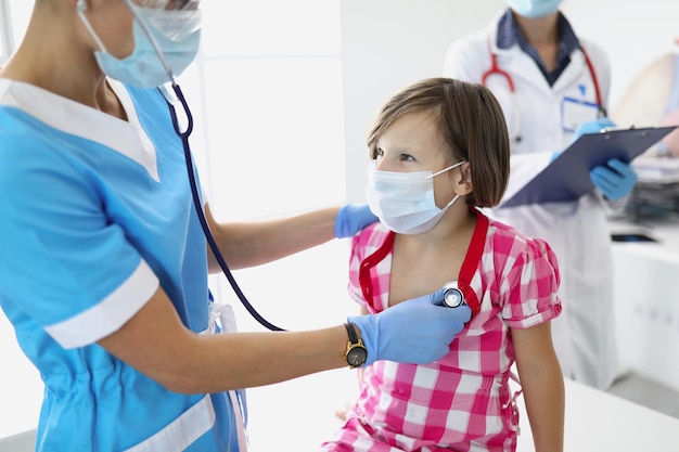 Portrait of child on doctors appointment qualified nurse listening kid with red stethoscope
