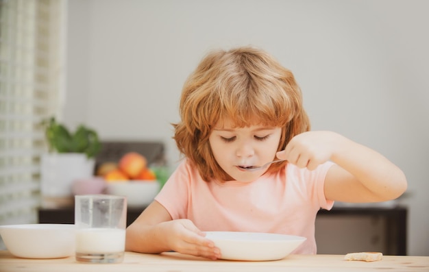 Portrait of child eating soup meal or breakfast having lunch by the table at home with spoon kids he