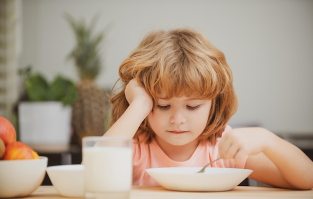 Portrait of child eating soup meal or breakfast having lunch by the table at home with spoon kids he