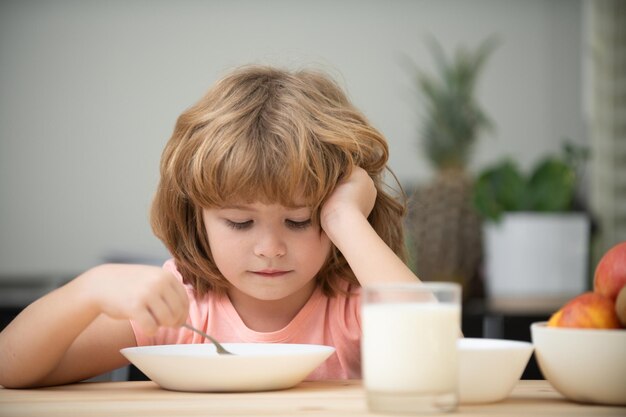 Portrait of child eating soup meal or breakfast having lunch by the table at home with spoon. Kids healthy food.