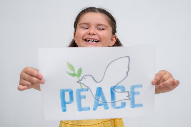 Portrait of a child girl with a poster dove of peace on a gray background