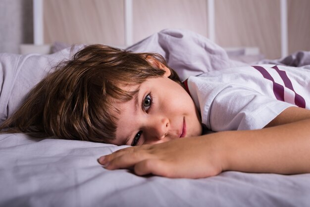 ベッドの上の綿のベッドリネンの上に横たわっているパジャマの子供の肖像画
