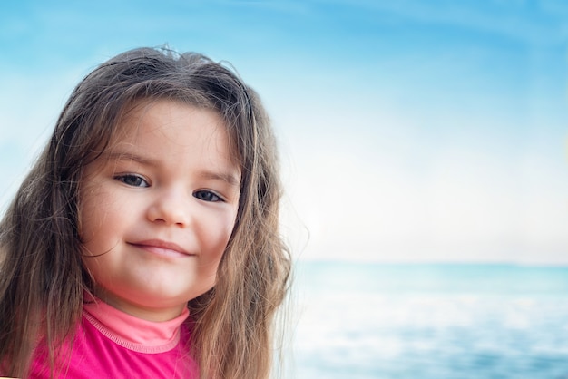 Portrait of a child at sea. girl on a background of blue sky and sea in a pink swimsuit