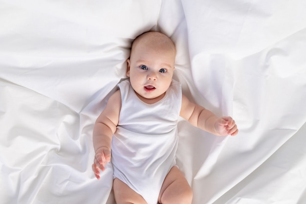 Portrait of a child on a white bed in the morning. Textiles and bed linen for children. A newborn baby has woken up or is going to bed