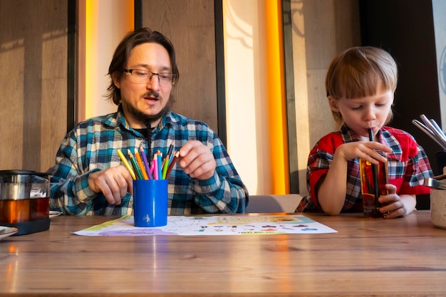 Portrait of child with his father drawing with pencils in cafe