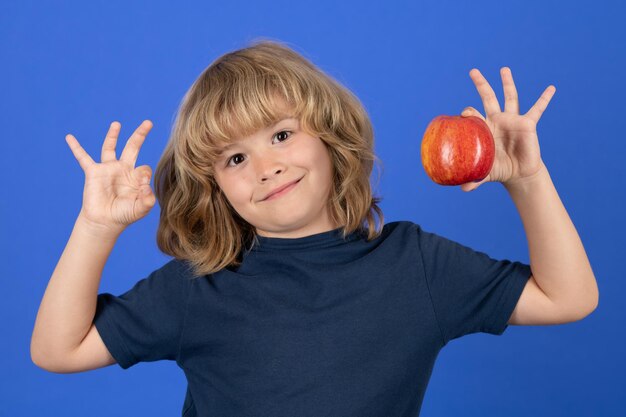 Portrait of a child with ok sign gesture hold a red apple on blue studio isolated background