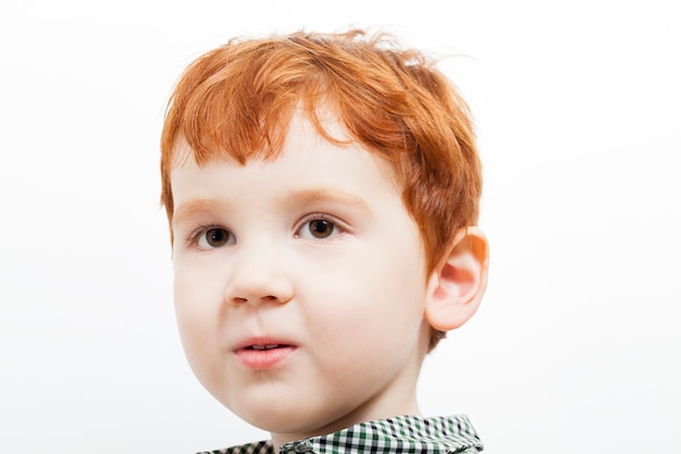 Ritratto di un bambino con i capelli rossi e le lentiggini sul viso, occhi marroni, su sfondo chiaro