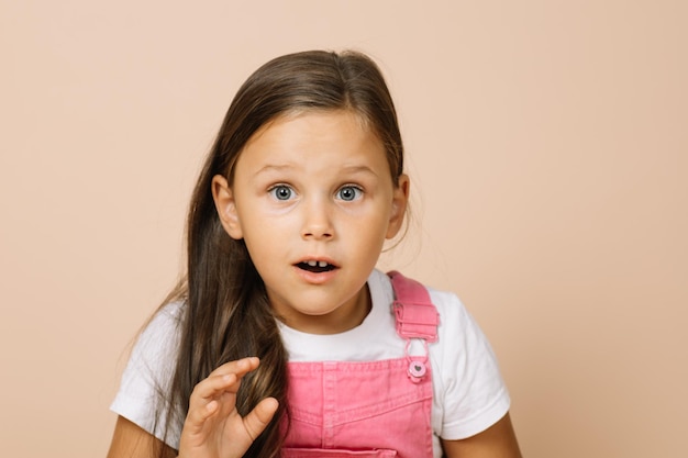 Portrait of child with surprised round eyes slightly opened mouth and raising hand looking at camera...