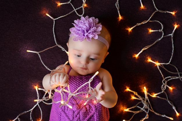 Photo portrait of a childgirl on a purple background with a garland which lies and examines the lights