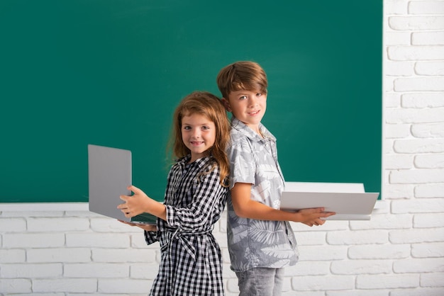 Portrait of children boy and girl with laptop computer and book at school kids in class on blackboard