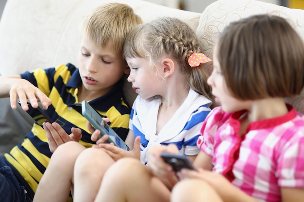 Portrait of children playing on mobile phone kids spending fun time together sitting on comfy