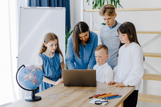 Portrait of children and teacher looking at laptop in the classroom