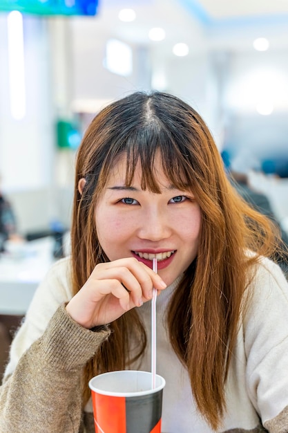 portrait of chinese young adult drinking a soft drink sitting in a shop after shopping