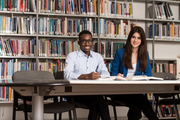 Portrait Of Clever Students With Open Book Reading It In College Library  Shallow Depth Of Field