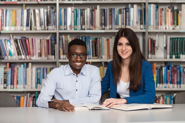 Portrait Of Clever Students With Open Book Reading It In College Library  Shallow Depth Of Field