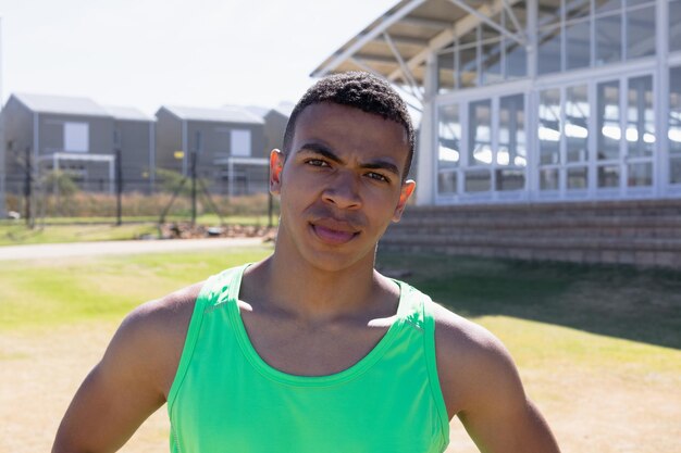 Portrait close up of a mixed race male runner training at a sports field, wearing a green vest, looking straight to camera