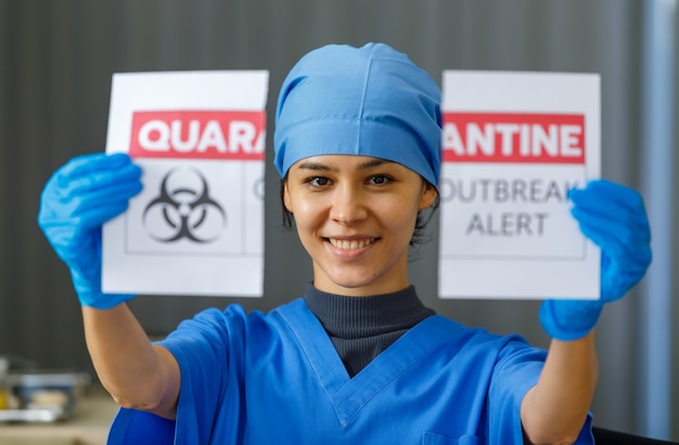 코로나바이러스 전염병이 끝나고 정상적인 삶과 사업이 돌아왔을 때 파란색 병원 유니폼 눈물 검역 발생 경고 용지를 입은 행복한 아름다운 의사의 초상화를 클로즈업합니다.