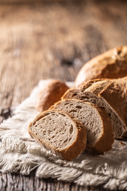 Portrait close up of slices of crusty bread leaned against the loaf on a vintage cloth and rustic wood.