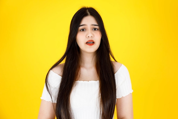 Portrait close up studio shot of asian young beautiful sexy\
long black hair female model wearing dental care teeth braces and\
crop top outfit standing smiling look at camera on yellow\
background.