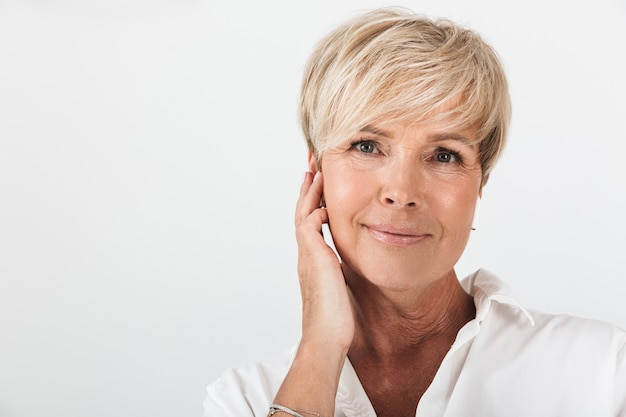 Portrait closeup of beautiful adult woman with short blond hair wearing earpods isolated over white wall in studio