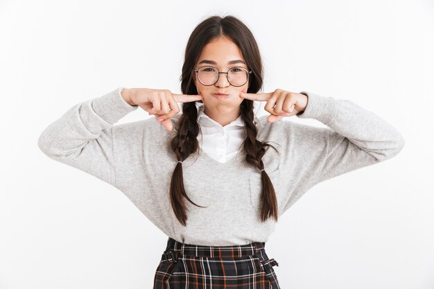 Portrait closeup of funny teenage girl wearing eyeglasses touching her cheeks while holding breath isolated over white wall