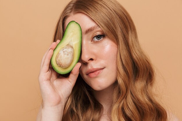 Portrait closeup of gorgeous young shirtless woman with long hair holding half of avocado fruit 