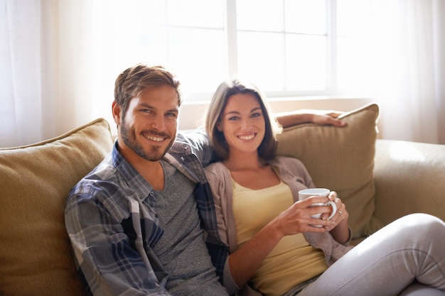 Portrait coffee and couple relax or smile on a couch together or bonding in the living room and with tea Man woman and love or affection with hot beverages or on a break and happy partners at home
