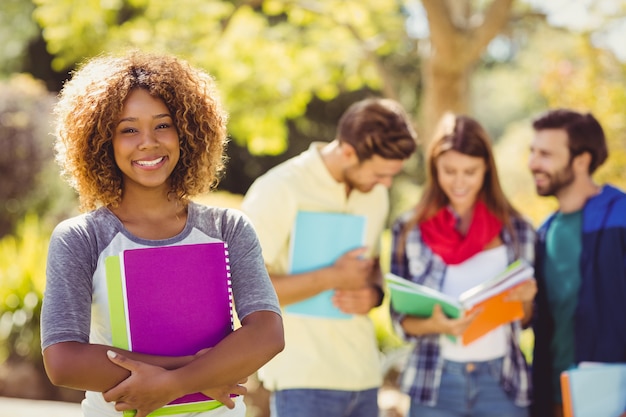 Portrait of college girl holding notes with friends in background