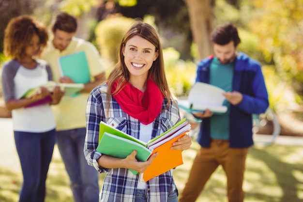 Portrait of college girl holding notes with friends in background