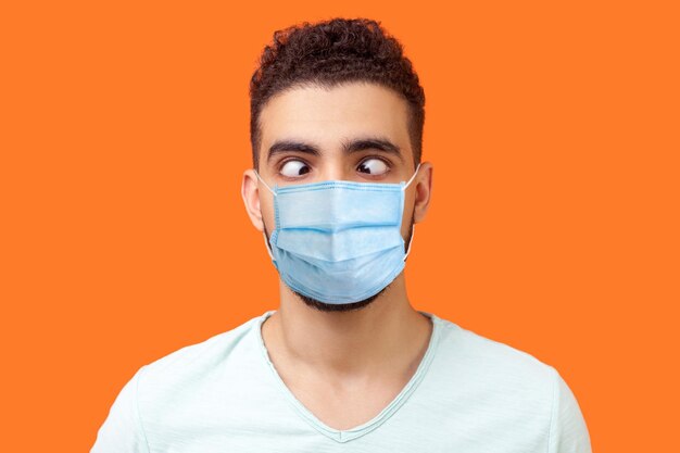 Portrait of comic crazy positive brunette man with surgical medical mask looking cross-eyed, having fun with silly face expression, playing fool. indoor studio shot isolated on orange background