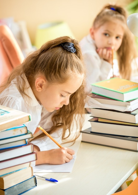 Portrait of concentrated girl doing homework while classmate trying to write off