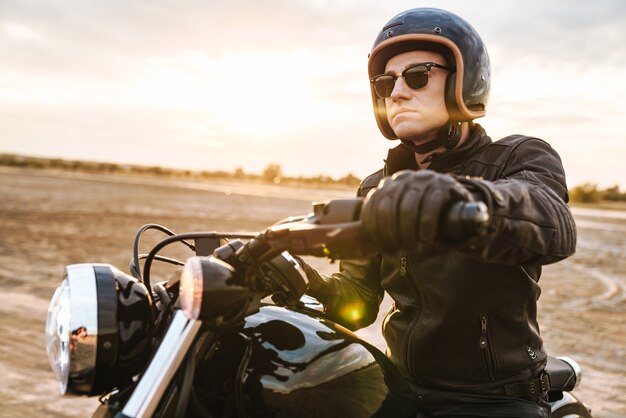 Photo portrait of concentrated serious young man biker on bike outdoors at the desert field.