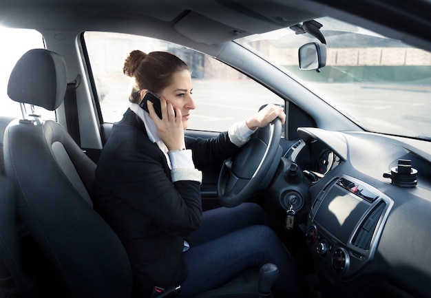 Портрет сосредоточенной женщины разговаривает по телефону и за рулем автомобиля
