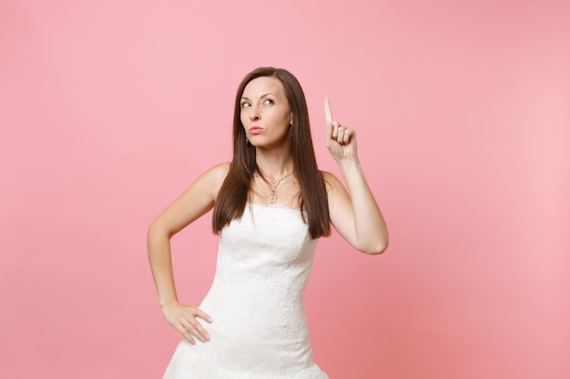 Portrait of concerned strict woman in elegant white dress standing pointing index finger up