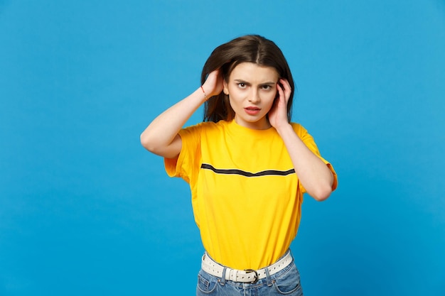 Portrait of concerned young woman in vivid casual clothes looking camera and putting hands on head isolated on bright blue wall background in studio. People lifestyle concept. Mock up copy space.