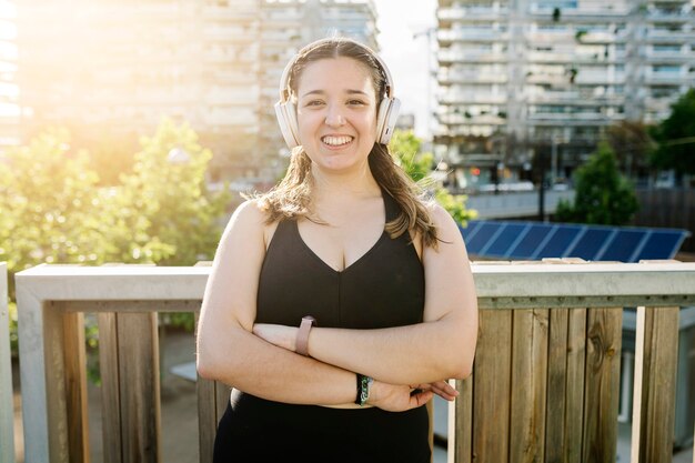 Portrait of confidence young curvy woman in sportswear with crossed arms smiling at camera outdoor