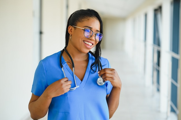 Ritratto fiducioso afroamericano medico femminile medico professionista scrittura note paziente isolate su priorità bassa di finestre corridoio clinica ospedale. espressione positiva del viso