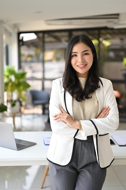 Photo portrait of a confident asian businesswoman stands with arms crossed in the office