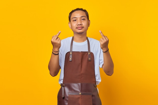Портрет уверенного в себе азиатского молодого человека в фартуке, показывающего средний палец с неуважением