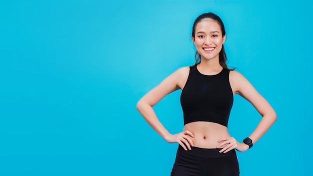 Portrait of confident beautiful asian fitness woman standing after exercise isolated on blue wall