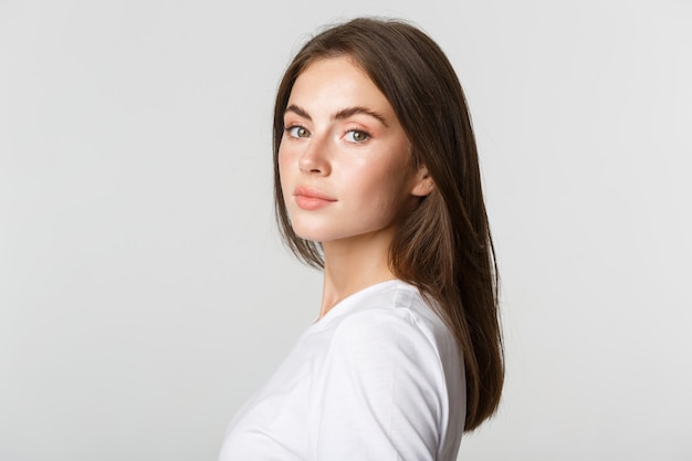 Portrait of confident beautiful brunette woman turning face at camera with dreamy look, white.