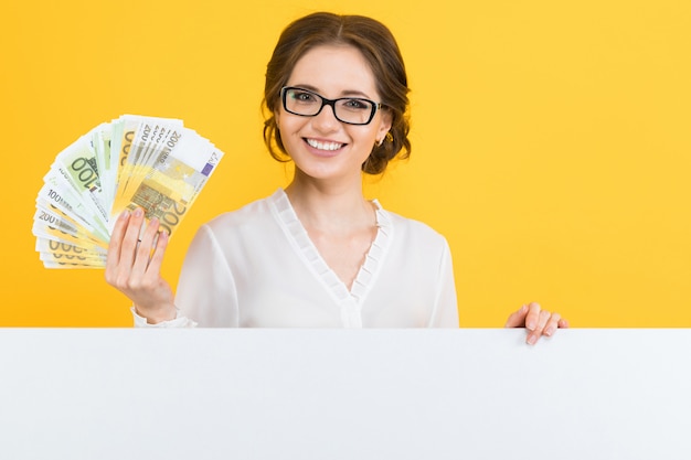 Portrait of confident beautiful young business woman with money in her hands and blank billboard