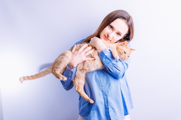 Portrait confident beautiful young woman hugging her orange cat in white background. animal care concept. love to the animals. animalistic