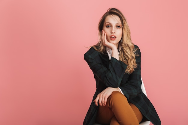 Portrait of confident businesswoman wearing jacket sitting in chair isolated on pink