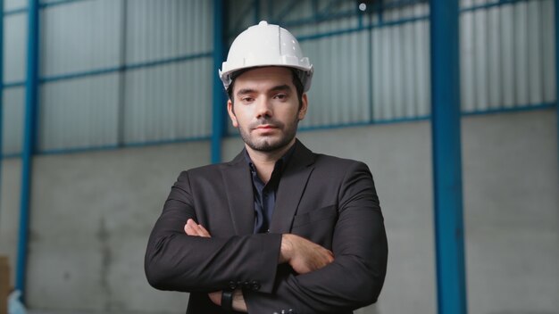 Портрет уверенно управляющего фабрикой в костюме и защитной каске на фабрике. Промышленно-инженерная концепция.